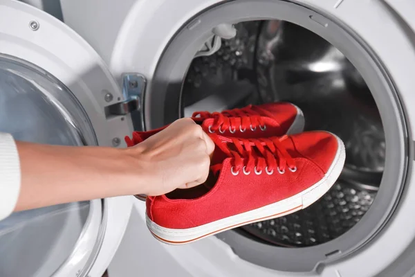 Mujer poniendo zapatillas rojas en la lavadora, primer plano — Foto de Stock