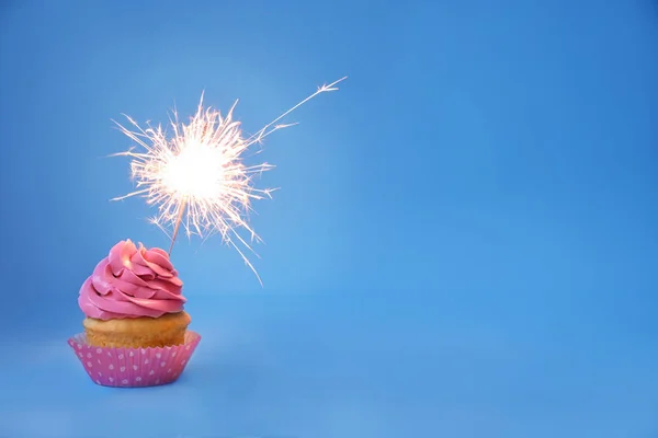 Delicious cupcake with sparkler on color background