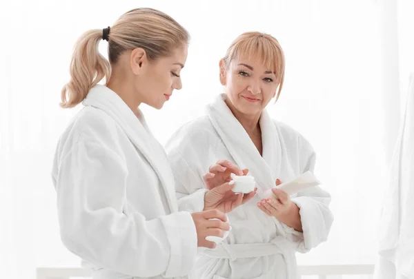 Rijpe vrouw en haar dochter die met behulp van cosmetische producten in badkamer — Stockfoto