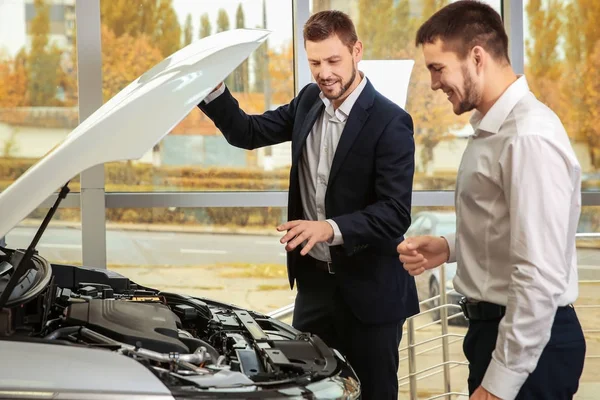 Stilig bilförsäljare med praktikanten tittar automobile motor i återförsäljaravtalet centrum — Stockfoto