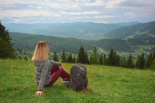 Női turisztikai ül a zöld fű, hegyek — Stock Fotó
