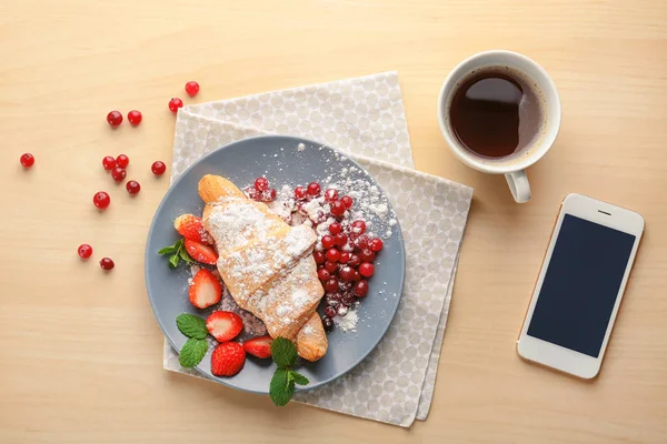 Composition with tasty croissant, coffee and mobile phone on wooden background — Stock Photo, Image