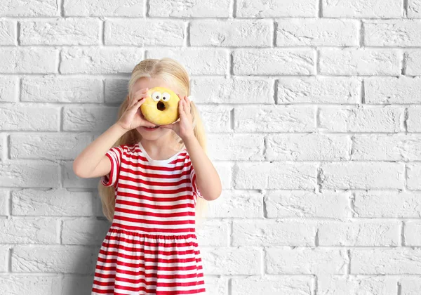 Little girl with sweet donut near white brick wall — Stock Photo, Image