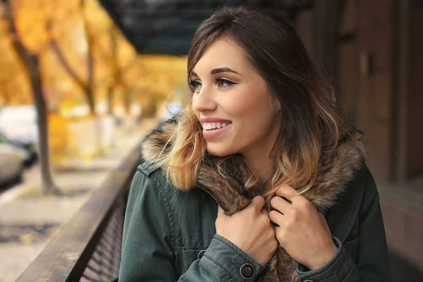 Привлекательная улыбающаяся женщина в куртке с меховым воротником на открытом воздухе — стоковое фото