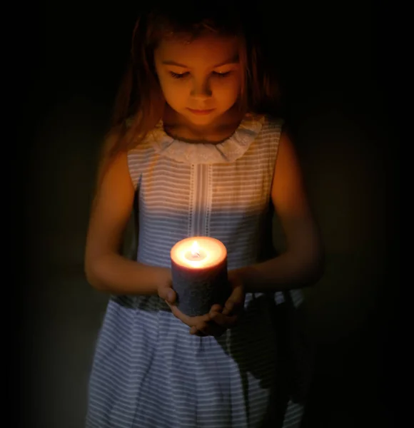 Little girl holding burning candle in darkness — Stock Photo, Image