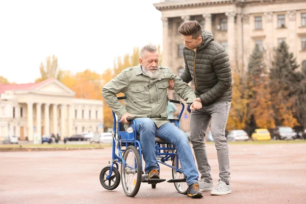 男子帮助他的年迈的父亲从轮椅上起床户外 — 图库照片