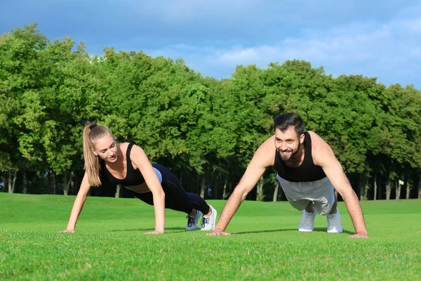 Young sporty couple doing exercise in green park — Stock Photo, Image