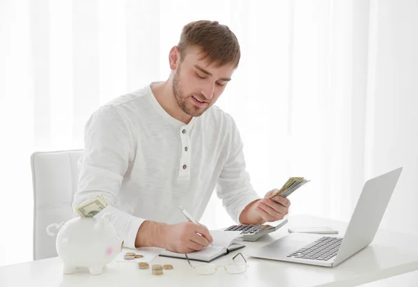 Jovem contando dinheiro à mesa dentro de casa — Fotografia de Stock