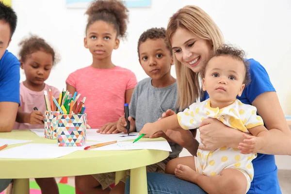 Молода жінка-доброволець малює з маленькими дітьми за столом. Концепція волонтерства за кордоном — стокове фото