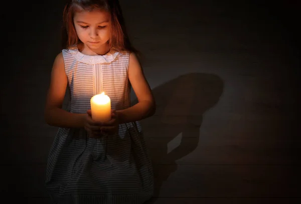 Little girl holding burning candle in darkness — Stock Photo, Image