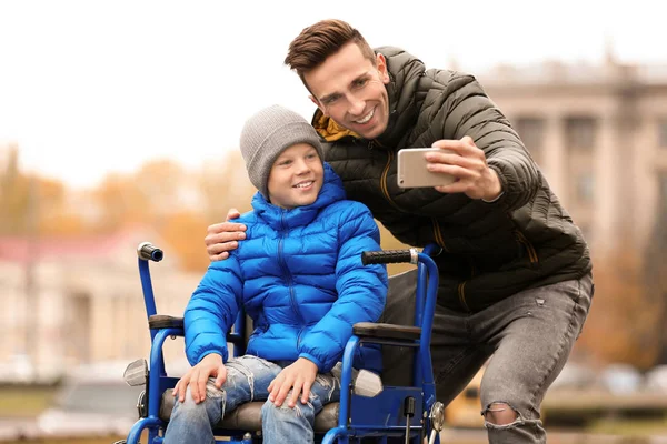 Az ember fia, kerekesszékkel vesz selfie szabadban őszi nap — Stock Fotó