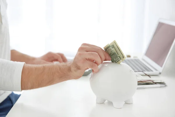 Young man putting money into piggy bank, closeup — Stock Photo, Image