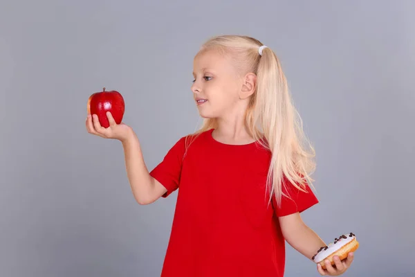 Petite fille avec pomme fraîche et beignet sucré sur fond gris — Photo