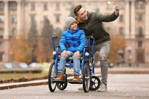 Homme avec son fils en fauteuil roulant prenant selfie à l'extérieur le jour de l'automne — Photo