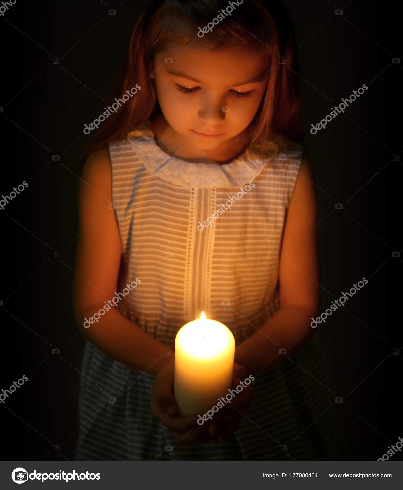 Little girl holding burning candle in darkness Stock Photo by