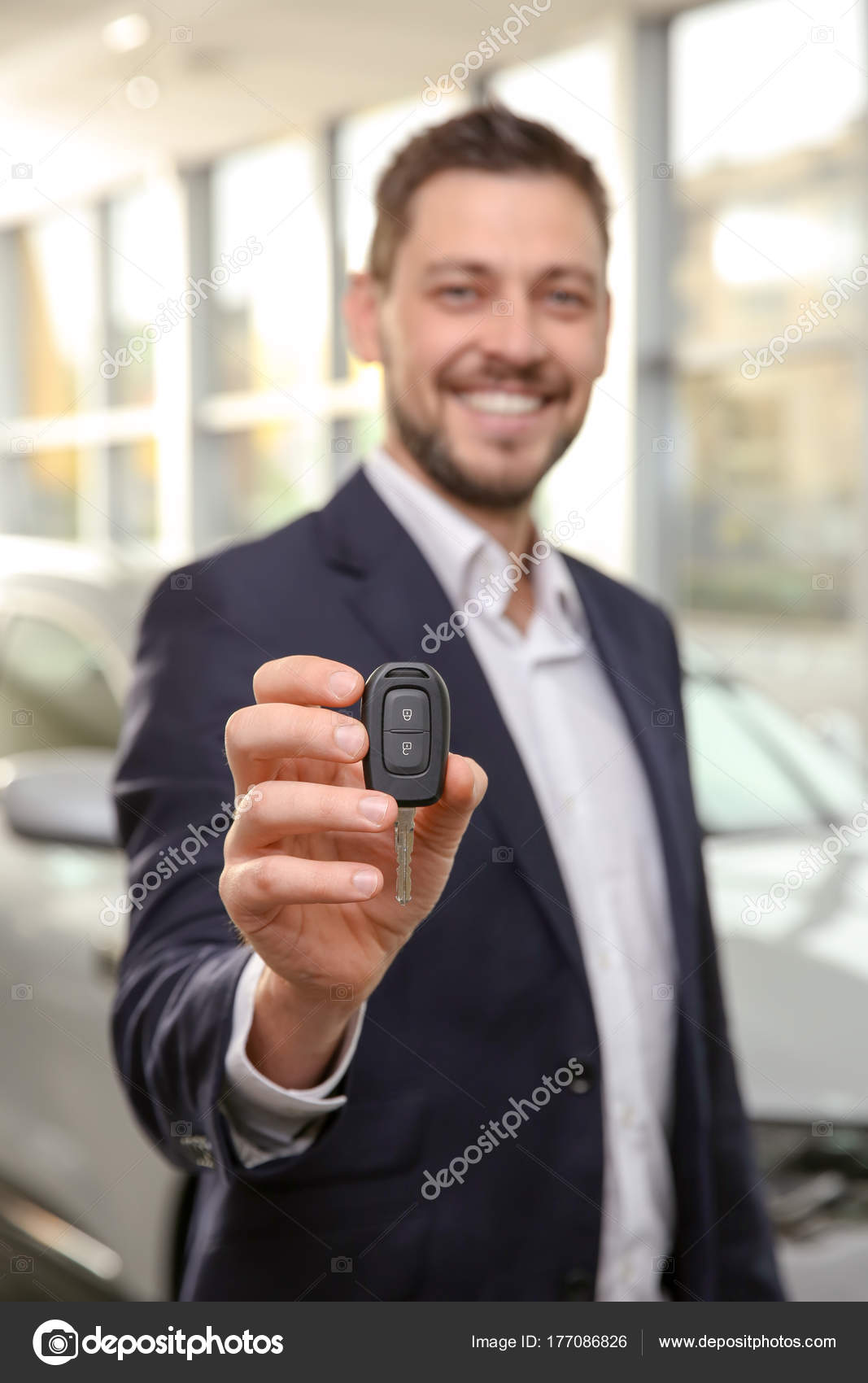 Handsome car salesman holding key in dealership centre Stock Photo by