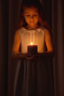 Küçük kız karanlıkta yanan mum tutan