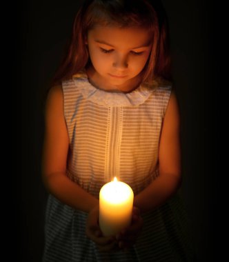 Küçük kız karanlıkta yanan mum tutan