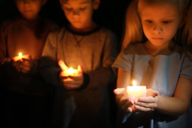 Küçük çocuklar karanlıkta yanan mum tutan
