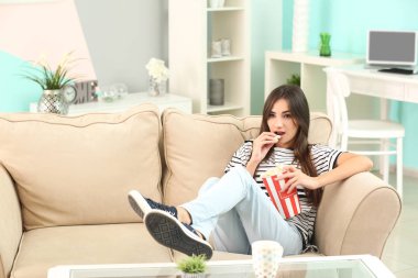 Genç kadın evde kanepenin üzerinde patlamış mısır yemek