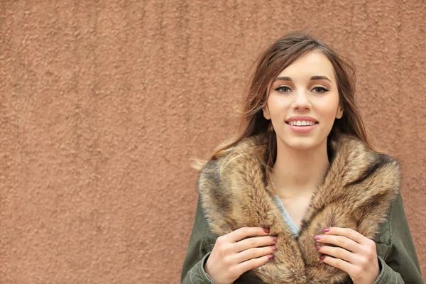 Mulher sorridente atraente na jaqueta com gola de pele no fundo marrom — Fotografia de Stock