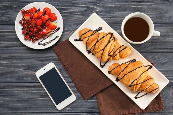 Composition with tasty croissants, coffee and mobile phone on wooden background — Stock Photo, Image