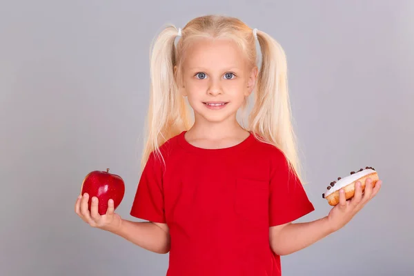 Meisje met verse appel en zoete donut op grijze achtergrond — Stockfoto
