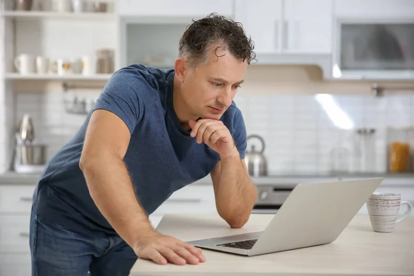 Bello uomo maturo che utilizza il computer portatile in cucina — Foto Stock