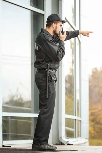 Gardien de sécurité masculin utilisant un émetteur radio portable près du bâtiment à l'extérieur — Photo