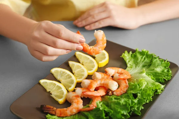 Mulher segurando camarão saboroso sobre placa na mesa — Fotografia de Stock