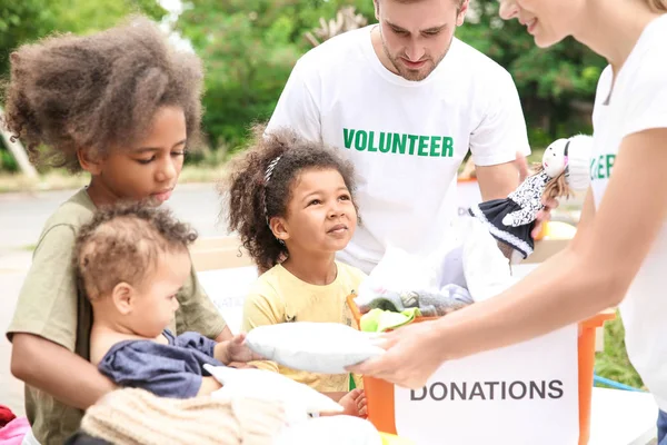 Voluntarios compartiendo ropa y juguetes con niños africanos pobres al aire libre — Foto de Stock