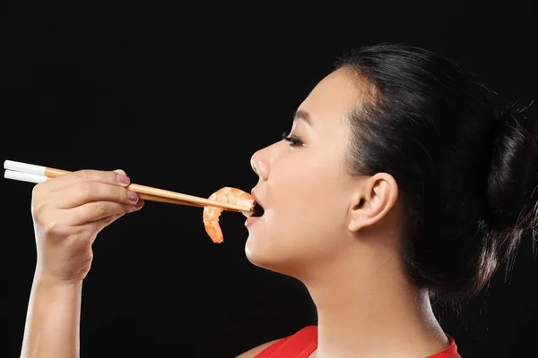 Beautiful Asian woman eating shrimp on black background — Stock Photo, Image