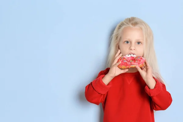 Маленькая девочка ест сладкий пончик на цветном фоне — стоковое фото