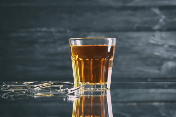 Glas en handboeien op tafel. Alcohol afhankelijkheid concept — Stockfoto