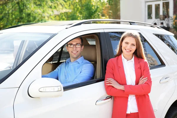 Man zit in de bestuurdersstoel en jonge vrouw stond in de buurt van de auto buiten — Stockfoto