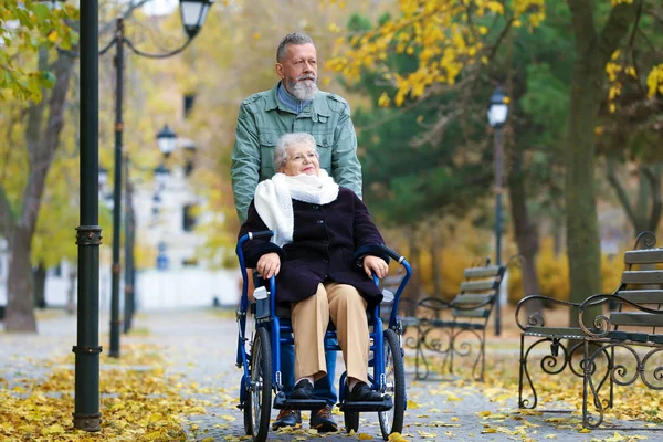 Homme âgé avec sa femme en fauteuil roulant à l'extérieur le jour de l'automne — Photo