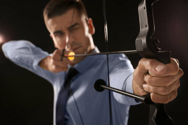 Young businessman practicing archery on dark background
