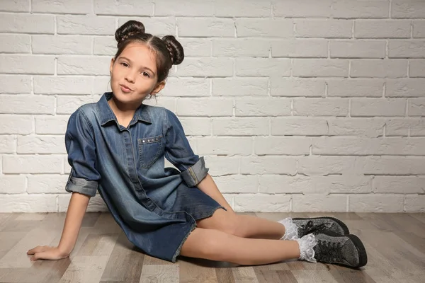 Adorável menina elegante sentado e posando perto da parede de tijolo — Fotografia de Stock