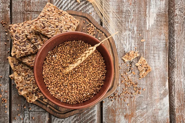 Tigela com trigo sarraceno cru e pão de semente em tábua de madeira — Fotografia de Stock