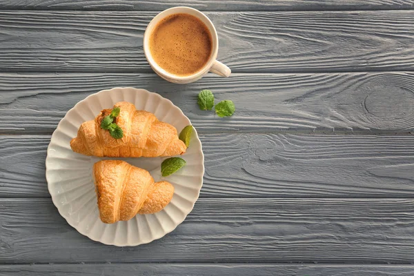 Plate with tasty croissants and cup of coffee on wooden background — Stock Photo, Image