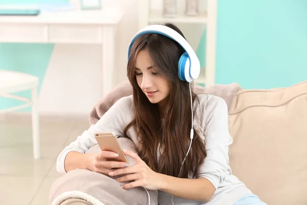 Jonge vrouw, luisteren naar muziek via een koptelefoon op de sofa thuis — Stockfoto