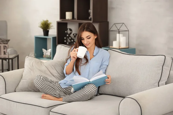 Junge Frau liest Buch zu Hause auf dem Sofa — Stockfoto