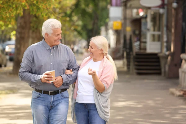 Starší pár s šálky kávy chůzi spolu venku — Stock fotografie