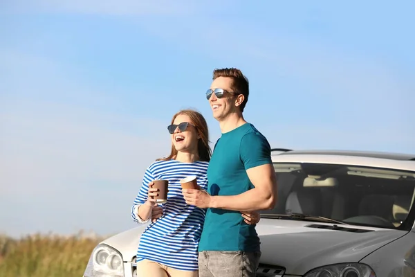 Vackra unga par med kaffe stående nära bil utomhus — Stockfoto