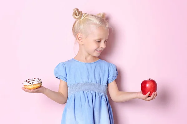 Menina com donut doce e maçã fresca no fundo de cor — Fotografia de Stock