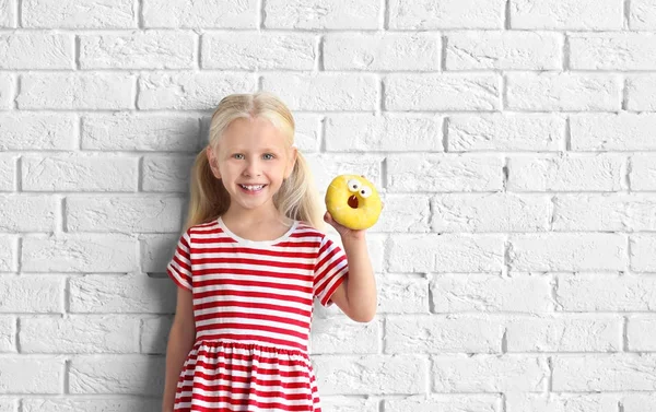 Little girl with sweet donut near white brick wall — Stock Photo, Image
