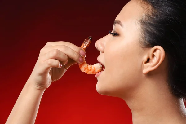 Beautiful Asian woman eating shrimp on color background — Stock Photo, Image