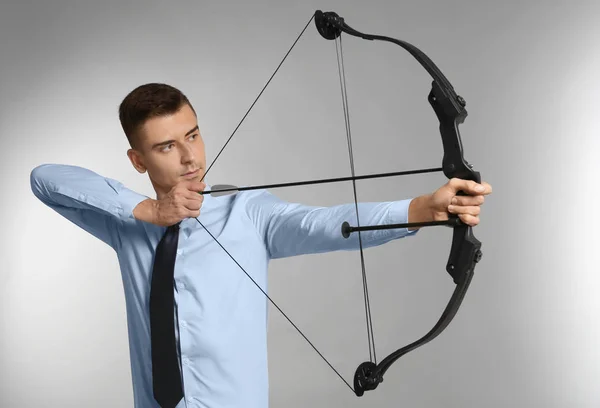 Giovane uomo d'affari che pratica tiro con l'arco su sfondo grigio — Foto Stock