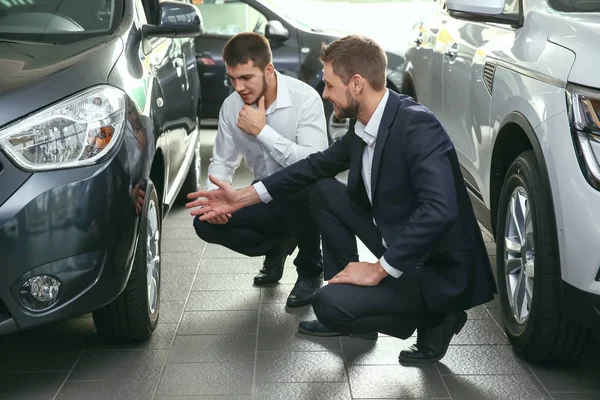 Bellissimo venditore di auto con tirocinante guardando l'automobile nel centro di concessionaria — Foto Stock