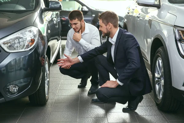 Bonito vendedor de carros com estagiário olhando para o automóvel no centro de concessionárias — Fotografia de Stock